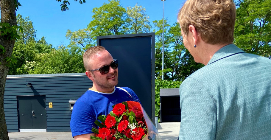Studiechef på sygeplejerskeuddannelsen Edel Marie Thomsen siger stort tillykke til Glenn. Glenn Michael Gandrup-Knudsen har en buket blomster i favnen og smiler til studiechef på sygeplejerskeuddannelsen på UC SYD, Edel Marie Thomsen